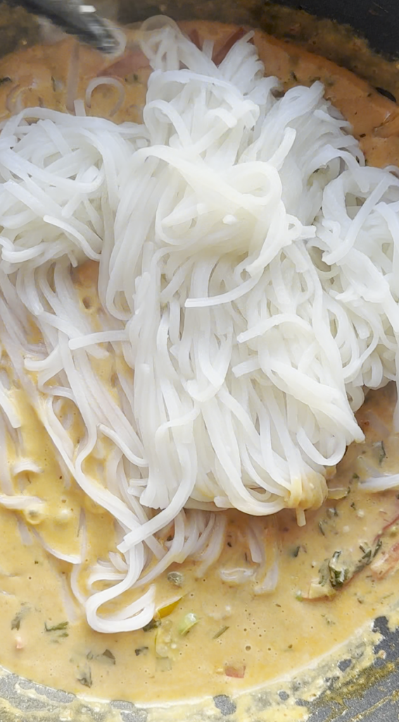 sliced bell peppers with cilantro, basil, and green onions added with garlic minced with coconut milk, Thai red curry paste, tomato paste, soy sauce all stirred together and rice noodles being added